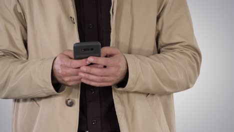 Man-in-trench-coat-using-mobile-smart-phone-on-gradient-background