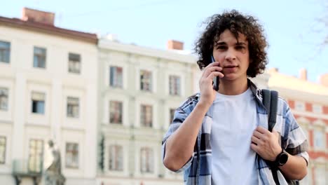 Un-hombre-está-hablando-por-teléfono-y-sonriendo.-Retrato-de-blogger-guapo,-estudiante-caminando-al-aire-libre-y-hablando-en-el-teléfono-inteligente-móvil.-Educación,-viajes,-concepto-de-turismo