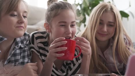 Chicas-adolescentes-bebiendo-café-y-comiendo-palomitas-mientras-ven-contenido-multimedia-en-el-ordenador-portátil