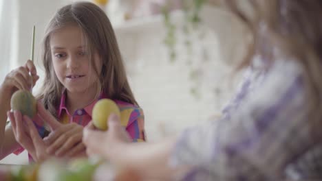 Female-hand-holding-Easter-egg-while-girl-painting-on-it-a-heart-with-a-brush-close-up.