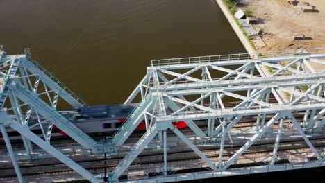 Luftaufnahme-der-Eisenbahnbrücke,-mit-einem-fahrenden-Zug-auf-ihr,-über-den-Fluss,-der-durch-eine-Großstadt-fließt