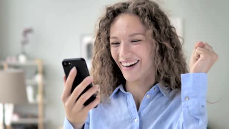 Excited-Curly-Hair-Woman-Enjoying-Success-while-Using-Smartphone