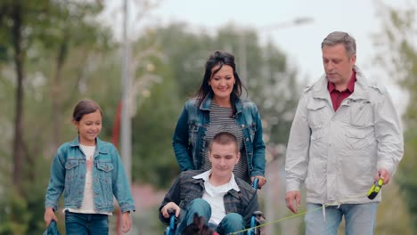 Perro-jugando-con-un-tipo-en-silla-de-ruedas.-Familia-amistosa-pasa-el-día-juntos,-un-adolescente-con-discapacidades.