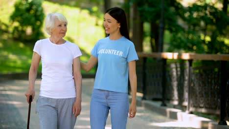 Mujer-voluntaria-y-paciente-de-la-tercera-edad-con-jardín-de-hospital-que-camina-palo,-cuidado