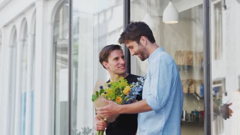 Pareja-gay-masculina-amorosa-sosteniendo-las-manos-saliendo-de-floristas-sosteniendo-un-montón-de-flores