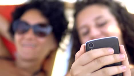 Teens-smile-preview-social-media-posts-on-smartphone-lying-on-beach-bed,-selective-focus