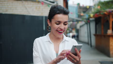 Excited-adult-woman-looking-at-smartphone-outdoors-after-getting-great-news