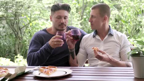 Gay-couple-having-pizza-for-lunch.-Swapping-glasses.