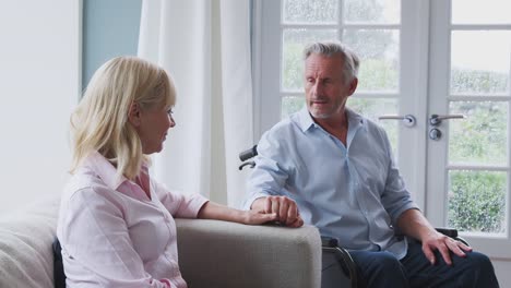 Senior-Paar-mit-Mann-im-Rollstuhl-sitzen-in-der-Lounge-zu-Hause-reden-und-lachen-zusammen