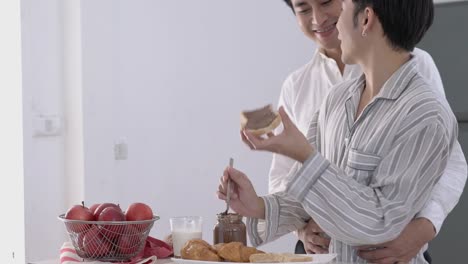 Asian-couple-gay-applying-chocolate-on-bread-in-morning-at-home.-Gay-boy-happy-emotion-and-hug-love-anniversary-together.-Concept-of-lifestyle,-family,-gay-and-bisexual.