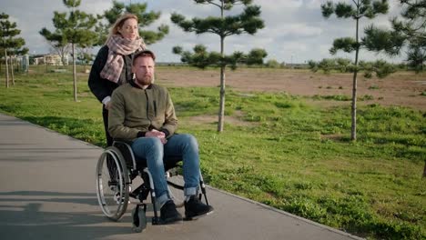 Man-is-sitting-in-invalid-carriage-and-his-wife-is-helping-him,-pushing-it