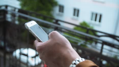 Mano-masculina-usando-el-teléfono-móvil-en-el-balcón