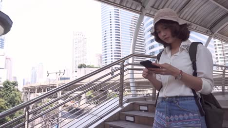 Slow-motion---Cheerful-Asian-backpacker-blogger-woman-using-smartphone-for-direction-and-looking-on-location-map-while-traveling-in-Bangkok,-Thailand.-Lifestyle-backpack-tourist-travel-holiday-concept