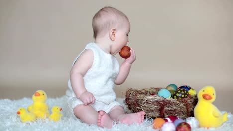 Lindo-niño-pequeño-niño,-jugando-con-huevos-de-pascua-de-colores-y-patos-decorativos-pequeños,-tiro-aislado,-fondo-beige