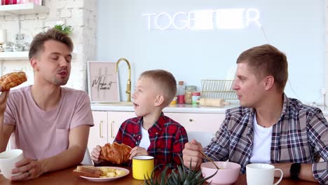 Feliz-familia-gay-dos-padres-e-hijo-están-desayunando-en-la-cocina.