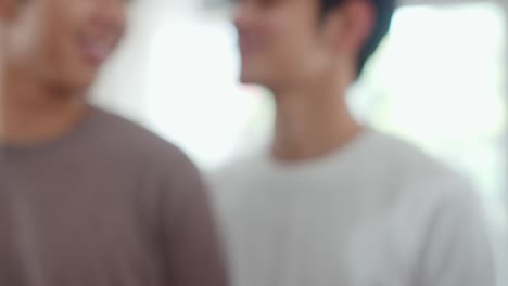 Portrait-Young-Asian-Gay-couple-feeling-happy-showing-ring-at-home.-Asia-LGBTQ+-men-relax-toothy-smile-looking-to-camera-while-hug-in-modern-living-room-at-house-in-the-morning-concept.-Close-up-Shot.