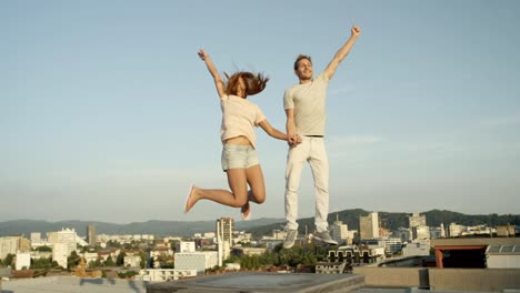 CLOSE-UP:-Two-lovers-holding-hands-and-jumping-on-rooftop-above-the-city