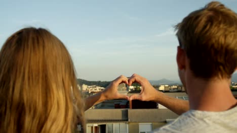 CLOSE-UP:-Young-girlfriend-and-boyfriend-on-rooftop-making-heart-shaped-symbol