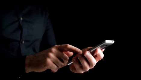 Concept,-digital-online-life-and-social-networks.-A-businessman-in-a-shirt-uses-his-smartphone-to-view-his-accounts.-Expressive-shot,-a-man-in-a-dark-room,-holding-a-stylish-phone