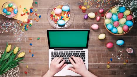 Man-using-laptop-computer-with-green-screen-on-table-decorated-with-easter-eggs-Top-view