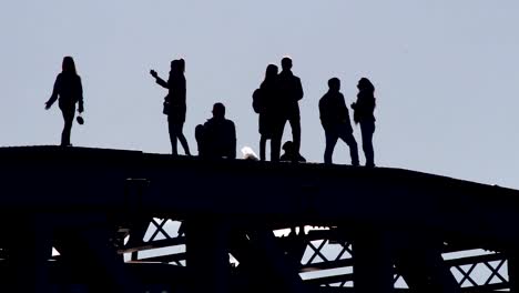 siluetas-de-jóvenes-paseando-y-tomando-fotos-de-cada-uno-en-una-situación-precaria-en-la-parte-superior-del-puente