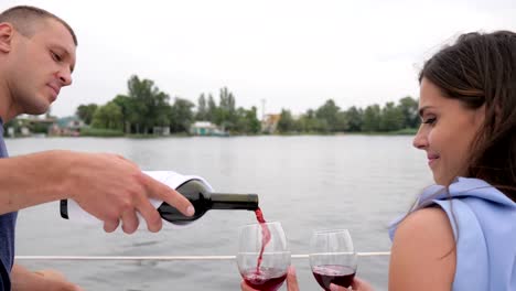 guy-pours-from-bottle-wine,-romantic-couple-drink-red-beverage-on-sea,-two-people-on-vacation,-glasses-in-hands-man