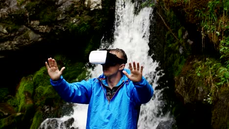 Un-hombre-utiliza-gafas-de-realidad-virtual-en-el-fondo-de-una-cascada-de-montaña