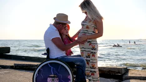 Disabled-father-in-wheelchair-and-little-daughter-listen-to-the-belly-of-pregnant-mother.disabled-men-and-happy-family