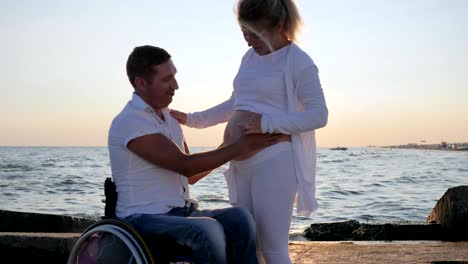 Love,-disabled-man-with-pregnant-female-at-sunset,-disabled-man-sitting-and-touching-big-tummy-women