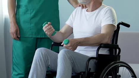 Aged-man-sitting-in-wheelchair,-holding-dumbbells,-talking-to-nurse,-recovery