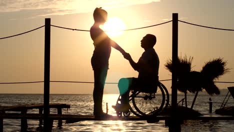 silhouette-of-female-and-male-handicapped-on-wheel-chair-holding-arms-and-look-at-horizon-in-sea