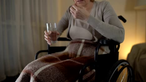 Sad-old-woman-in-wheelchair-taking-medicine,-recovery-period,-depression