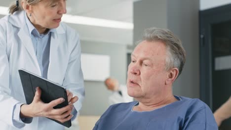 En-el-Hospital-femenino-médico-muestra-Tablet-PC-al-paciente-mayor,-explicando-su-condición.-Moderno-Hospital-con-la-mejor-atención-posible.