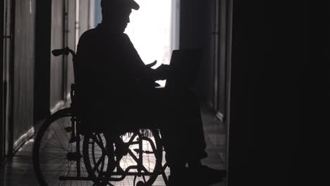 Silhouette-of-Disabled-Man-on-Wheelchair-Using-Laptop-and-Smartphone