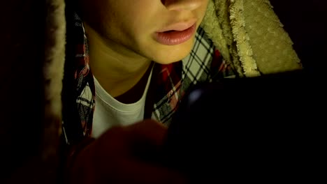 Boy-scrolling-social-networks-on-tablet-night-under-blanket,-internet-addiction