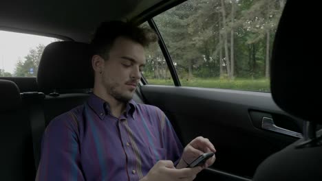 Young-entrepreneur-man-sitting-in-a-back-of-riding-uber-cab-texting-and-chatting-on-his-smartphone