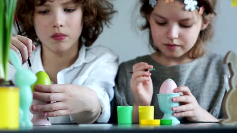 Cerca-de-retrato-de-un-niño-y-una-niña-con-pinturas-y-pinceles.-Creatividad-de-Pascua-infantil.-Hermano-y-hermana-decoran-huevos-de-Pascua-y-reír-alegremente