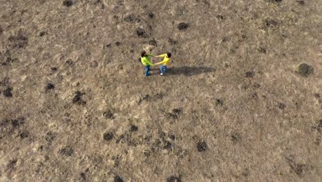 Aerial-4k-view-of-two-girlfriends-holding-hands,-rotating-in-a-meadow-by-drone