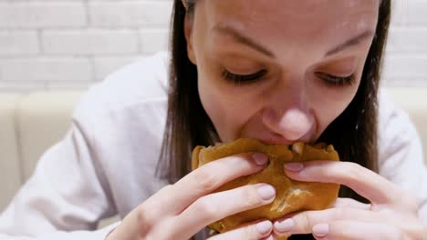 Woman-eating-a-hamburger-with-relish-and-delight-in-cafe.