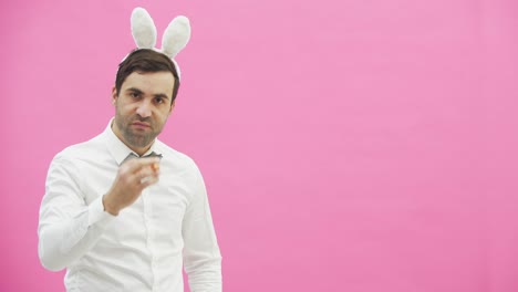 Young-handsome-boy-standing-on-a-pink-background.-A-man-with-rabble-ears-on-his-head.-A-man-holding-a-carrot-puts-it-in-his-mouth-and-reproduces-the-movements-of-a-cigarette.-Throwing-the-carrot-goes-out-of-the-frame.