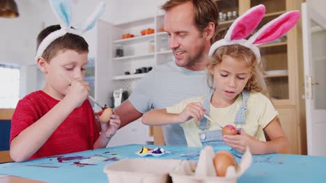 Vater-mit-Kindern,-die-Kaninchen-tragen,-dekoriert-Ostereier-zu-Hause-zusammen