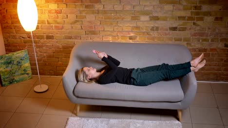 Primer-plano-de-tiro-retrato-de-joven-estudiante-usando-el-teléfono-y-acostado-en-el-sofá-descansando-en-el-interior-de-la-acogedora-casa