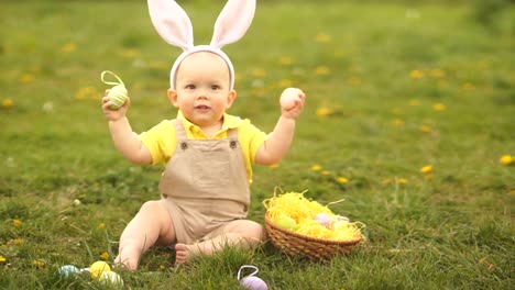 Schönes-Baby-in-einem-Osterhasen-Kostüm-sammelt-Ostereier-in-einem-Korb,-der-auf-dem-Rasen-im-Park-sitzt.-Frühlingshaftes,-glückliches-Osterfest