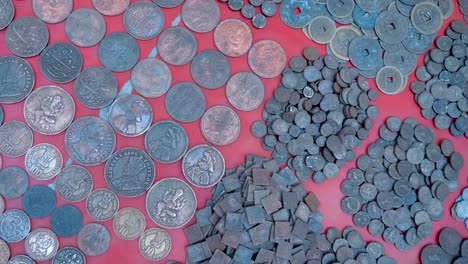 Vintage-Indian-coins-in-large-piles-lie-on-a-red-counter-in-Rishikesh,-India