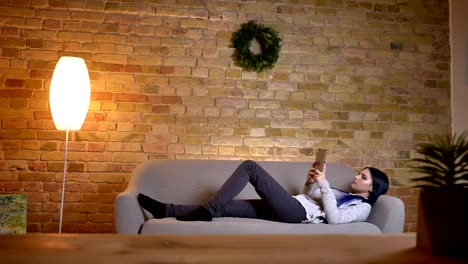 Closeup-shoot-of-young-pretty-caucasian-female-using-the-tablet-while-lying-on-the-couch-in-a-cozy-apartment