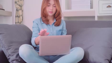 Asian-woman-working-on-laptop-in-living-room,-beautiful-female-feeling-tired-sleeping-lying-on-sofa-after-work-hard-at-home.-Women-working-at-home-concept.