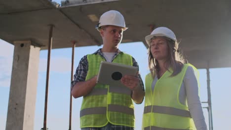 Supervisor-of-a-building-under-construction-man-discussing-with-engineer-designer-woman-the-progress-of-construction-and-examines-a-building-plan