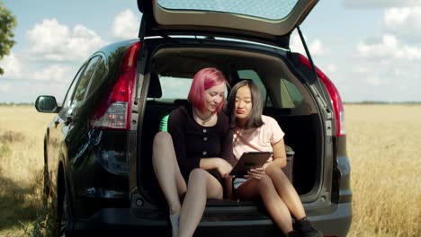 Female-travelers-using-tablet-pc-in-car-trunk