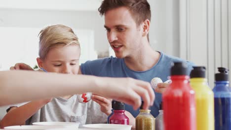 Padre-de-pie-junto-a-la-mesa-de-la-cocina-ayudando-a-los-niños-a-pintar-huevos-para-La-Pascua---tiro-en-cámara-lenta