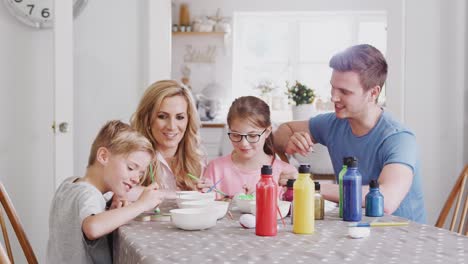 Familie-sitzt-um-Küchentisch-mit-Eltern-helfen-Kindern-Ostern-Dekorationen-zu-malen---in-Zeitlupe-gedreht